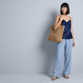 Woman in a navy satin top and jeans carrying a woven tote bag