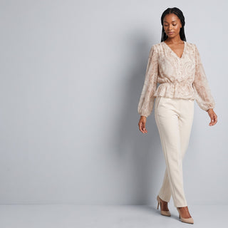 Woman in a blush ruffled blouse and cream trousers